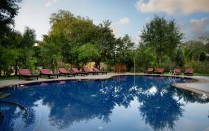 暹粒的住宿－Khemara Sovannphum Hotel，一座游泳池,后面设有红色椅子和树木