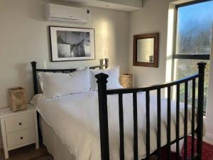 a bedroom with a bed with white sheets and a window at Deer Park Apartment CPT - With Sweeping Views in Cape Town