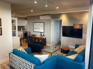 Deer Park Apartment CPT - With Sweeping Views في كيب تاون: غرفة معيشة مع أرائك زرقاء ومطبخ