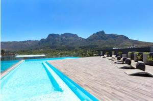 a swimming pool with chairs and mountains in the background at Newlands Peak - Spacious one-bed apartment in Cape Town