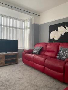 a living room with a red couch and a flat screen tv at Lovely 3 bedroom house with off street parking in Thornton