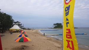 - une plage avec deux parasols et un panneau dans l'établissement 돼지민박 102호 진하해수욕장, à Ulsan