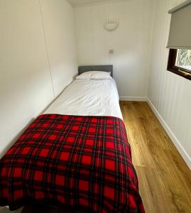 Ce lit se trouve dans un dortoir doté d'une couverture rouge et noire. dans l'établissement Lagavulin 3, à Portpatrick