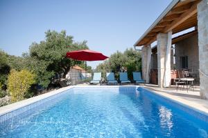 uma piscina com um guarda-sol vermelho, uma mesa e cadeiras em Island Villa Adriana with heated pool and sauna em Lun