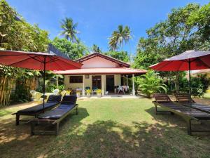 a patio with benches and umbrellas in front of a house at Mango Villa in Hikkaduwa
