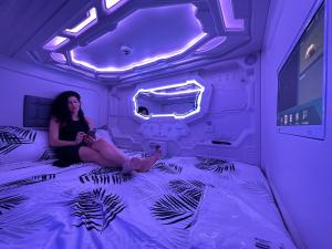una mujer sentada en una cama en una habitación púrpura en GOOD VIBES ONLY Capsule Hostel Malaga, en Málaga