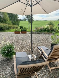two chairs and an umbrella on a gravel patio at Top modernes Appartement mit Blick ins Grüne in Kißlegg
