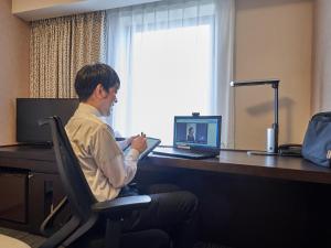 un hombre sentado en una silla frente a un escritorio con un portátil en Richmond Hotel Aomori, en Aomori