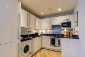 a kitchen with white cabinets and a washer and dryer at Glamorous Central Apartment in London