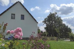 a white house with pink flowers in a yard at Storchennest - Ferienwohnung am Storchenradweg in Ketzür