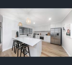 a white kitchen with a counter and stools in it at Brand New Luxury Abode on Shaw in Wagga Wagga