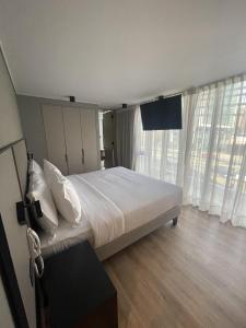 1 dormitorio con 1 cama grande con sábanas blancas y ventanas en One Manquehue Aparthotel, en Santiago
