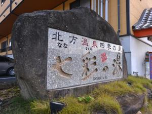 Un cartello su una roccia davanti a un edificio di 北方温泉四季の里　七彩の湯 a Takeo