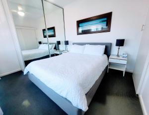 1 dormitorio con 1 cama blanca grande y espejo en Zig Zag at Henley ~ BEACH ~ DINING ~ WiFi ~Airport, en Henley Beach South