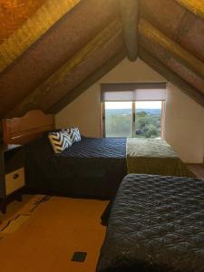 a attic bedroom with two beds and a window at Villa Serrana Cabaña Tata Ruben y Olga 2dormitorios in Villa Serrana
