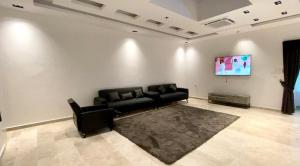 sala de estar con sofá negro y TV en La Vida Inn Quriyat, 
