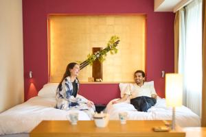 a man and woman sitting on beds in a hotel room at Hotel Resol Trinity Kanazawa in Kanazawa