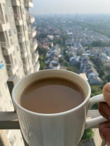 a person holding a cup of coffee in front of a window at apartemen bintaro icon in Pondokaren