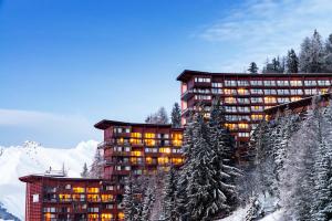 Un grand bâtiment avec des lumières allumées dans la neige dans l'établissement Lagrange Vacances Le Roc Belle Face, à Arc 1600