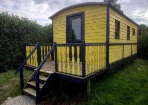 a small yellow house with a wooden porch at Roulotte et Jacuzzi de Rachel au Domaine du Reuze in Winnezeele