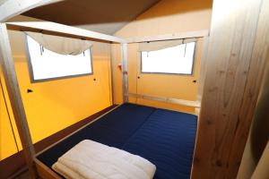 een kleine kamer met een blauw bed en 2 ramen bij De Zuidvliet Glamping Deluxe 1 in Wolphaartsdijk