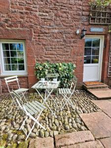 two chairs and a table in front of a brick building at Langriggs at Wetheral Cottages in Great Salkeld