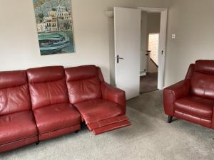 Large 2-bedroom maisonette with free parking في تويكنهام: أريكة جلدية حمراء وكرسيين في غرفة