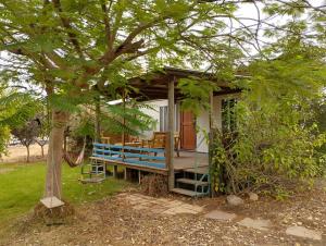 une petite maison avec une véranda et un arbre dans l'établissement ביתהבוצ - מקום טבעי למפגשים, à Talmei Yosef