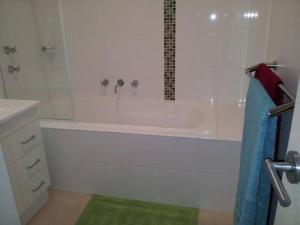 La salle de bains blanche est pourvue d'une baignoire et d'une douche. dans l'établissement Entire 2BR sunny house @Franklin, Canberra, à Canberra