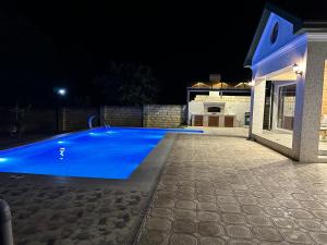 uma piscina azul à noite com uma casa em Katej em Quba