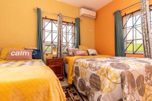 two beds in a room with orange walls and windows at J&R Sunshine Retreat in Spanish Town