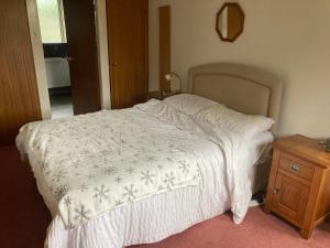 a bed with a white blanket and a wooden night stand at Lokiladdich in Bearsden