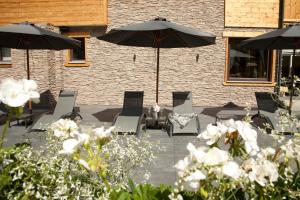 un patio con sillas, sombrillas y flores blancas en Hotel Die Montafonerin en Vandans