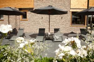 a patio with chairs and umbrellas and white flowers at Hotel Die Montafonerin in Vandans