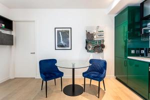a kitchen with a glass table and two blue chairs at Canary Wharf City Escape 1-Bed Apartment in London