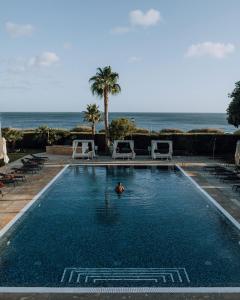 a person in a swimming pool next to the ocean at Grande Real Villa Itália Hotel & Spa in Cascais