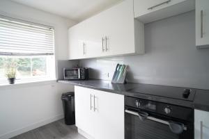 cocina con armarios blancos y microondas negro en Dunalastair Apartment, en Glasgow