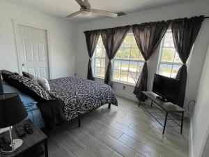 een slaapkamer met een bed, een televisie en 2 ramen bij Port Saint Lucie A Little Piece Of Heaven in Port Saint Lucie
