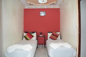 two beds in a room with a red wall at Riad el Boukhiri in Marrakech