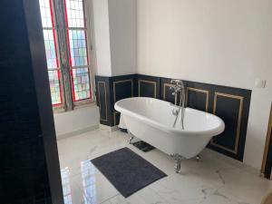 La salle de bains est pourvue d'une baignoire blanche et de fenêtres. dans l'établissement Manoir avec son parc de 12000m², à Chaumes-en-Brie