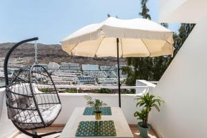 una sedia e un ombrellone su un balcone con tavolo di Canaima Corner with Heated Pool a Mogán