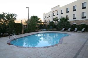 a pool in a courtyard with chairs and a building at Hampton Inn & Suites College Station in College Station