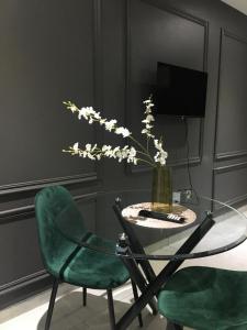 a glass table with a vase of flowers and two green chairs at Black Rose Guesthouse in Soweto