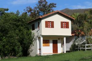 Casa blanca con ventanas marrones y valla en Chalé e Camping Elementais, en São Thomé das Letras