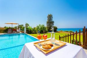 een tafel met twee drankjes en eten naast een zwembad bij Kalisto Beach Villa in Kato Yialia