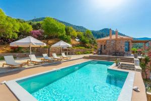 uma piscina com cadeiras e guarda-sóis em frente a uma casa em Villa Diona em Panormos