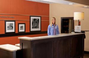 una mujer de pie detrás de un mostrador en una sala de espera en Hampton Inn & Suites Fargo Medical Center, en Fargo