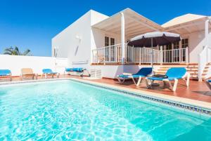 a villa with a swimming pool with chairs and an umbrella at Villa Tania in Puerto del Carmen