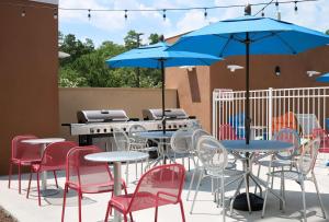 a patio with tables and chairs with a grill and blue umbrellas at Home2 Suites by Hilton Greenville Airport in Greenville