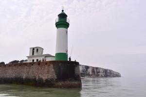 a green and white lighthouse sitting on the water at La Capitainerie in Le Tréport